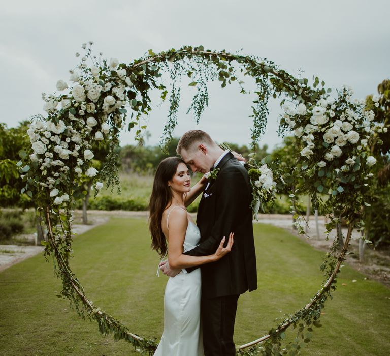 Bride and groom hug in front of their white altar flower display