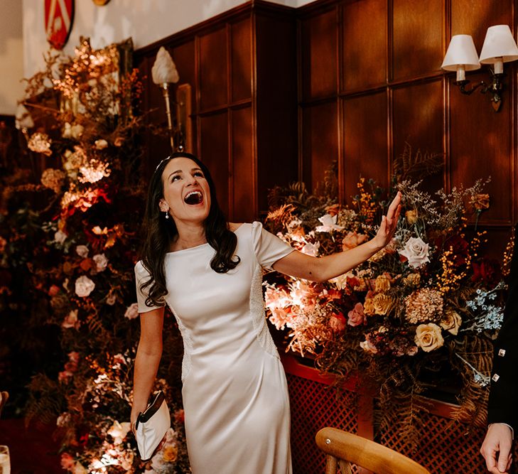 A bride and groom look up during wedding speeches and laugh. They are surrounded by Christmas church wedding flowers that they repurposed to their reception.