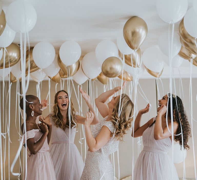 Portraits of the bride in sparkly bridal separates her bridesmaids in different chiffon dresses on the wedding morning playing with biodegradable helium balloons 