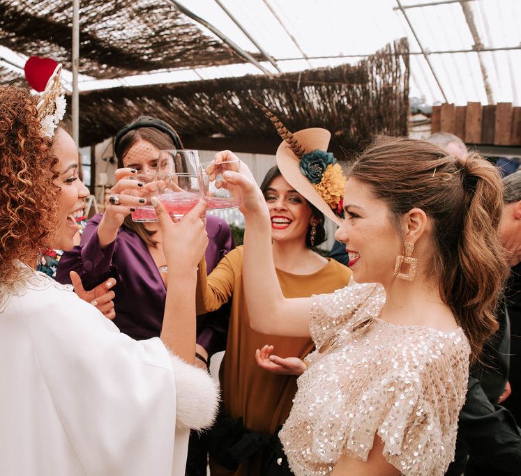 A bride with curly hair raises a drink with wedding guests