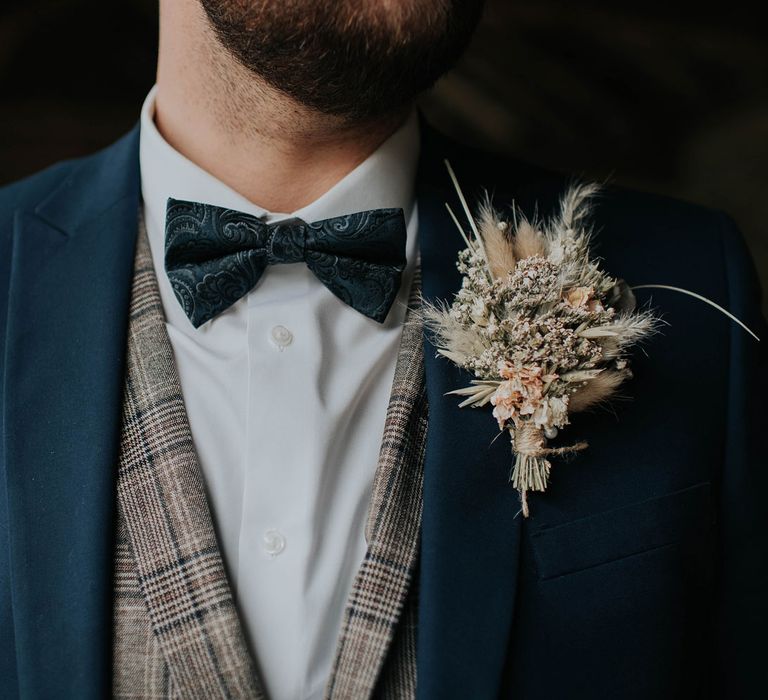 Groom in navy suit and tartan waistcoat with bow tie and dried flower buttonhole