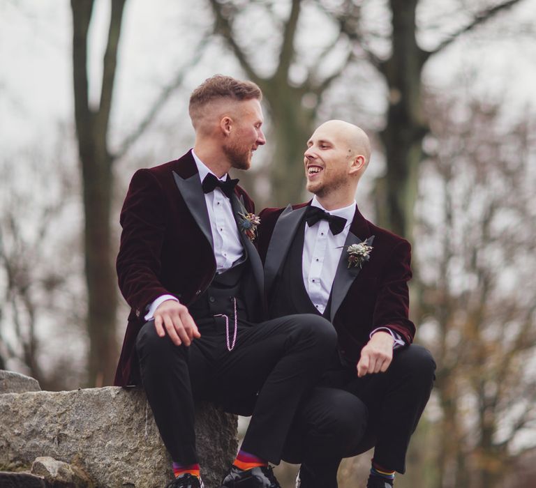 Portrait of gay couple in matching burgundy tuxedo jackets and rainbow socks 