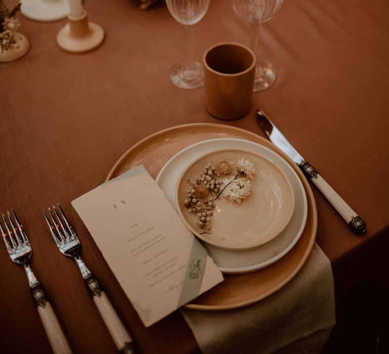 Place setting with coloured plate, menu card, dried flowers and ivory cutlery for boho elopement 