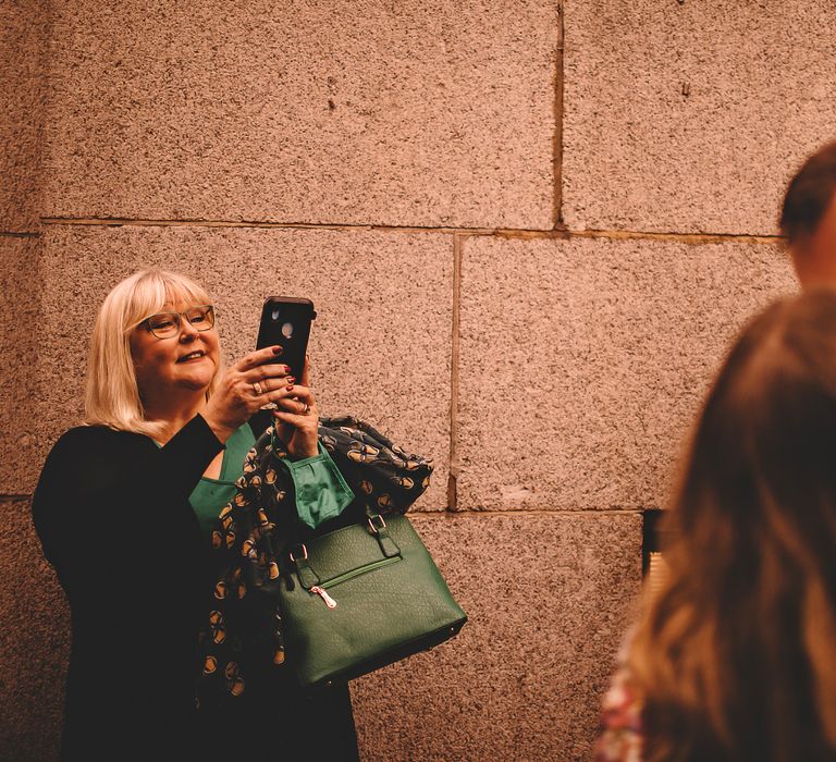 Bride & groom kiss as wedding guest takes photo on her phone