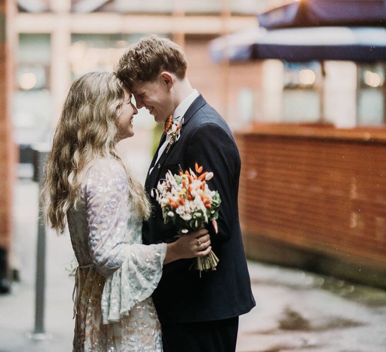 Bride and groom standing with their heads together smiling with white and peach wedding flowers