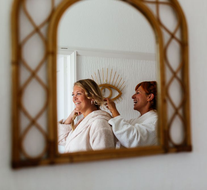 Brides smiling in mirror reflection wearing dressing gowns