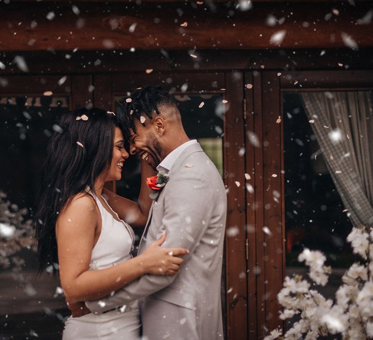 Bride & groom laugh together and confetti blows around them