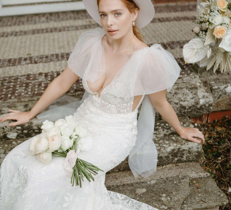 Bride wearing a blush pink stetson hat, puffed tulle shoulder wedding dress with plunge neckline and natural makeup