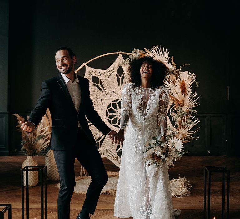 Bride & groom celebrate after ceremony in front of Macrame decor and pampas grass