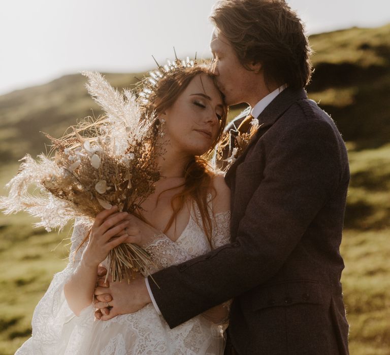 Bride leans into grooms chest whilst the sun shines behind them