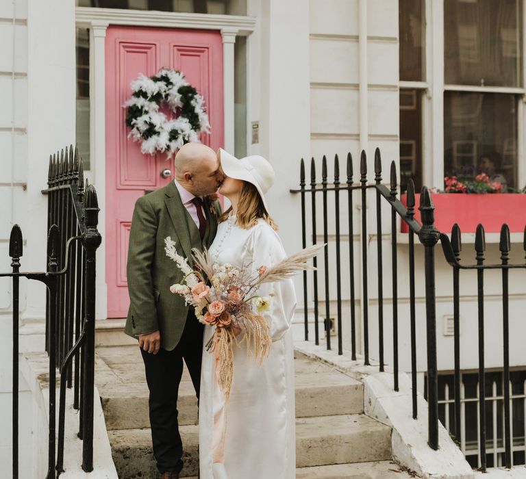 Bride & groom stand in front of pink door on their wedding day