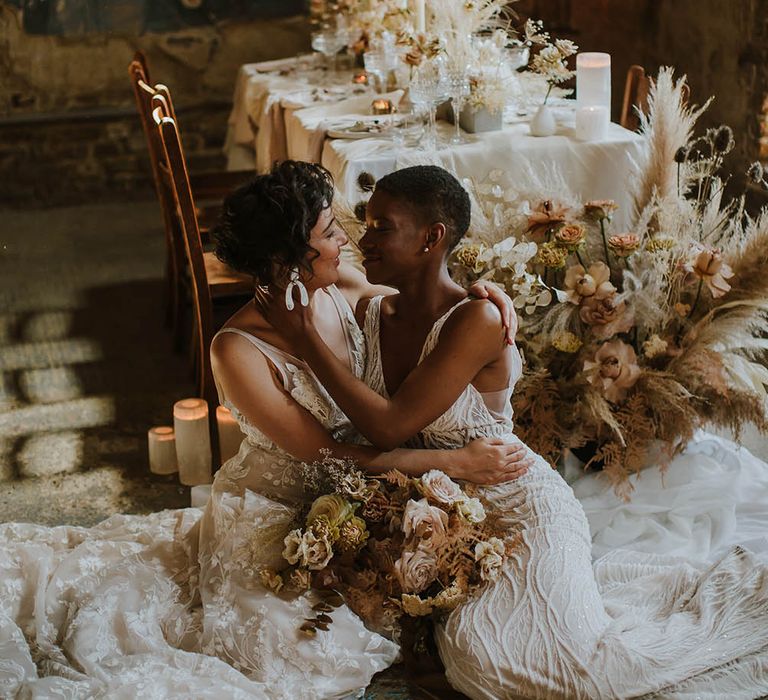 Two brides sitting on the floor at their Asylum London wedding reception with dried flower arrangements and candles 