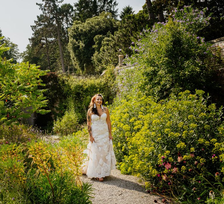 Boho bride in a strapless lace wedding dress and tassel earrings walking through the Walled Gardens at The Fig House, Middleton Lodge 