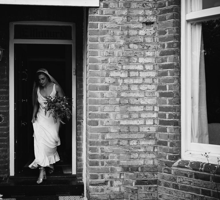 Bride in a satin Ghost wedding dress walking out of her home on the wedding morning 