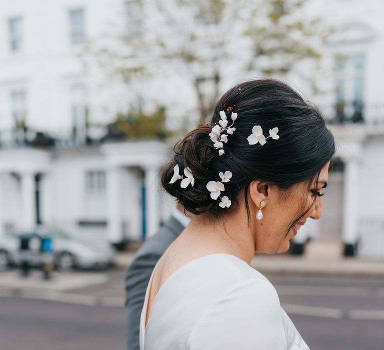 Bride wears her dark hair pulled back into low up-do complete with soft floral hair accessories in white