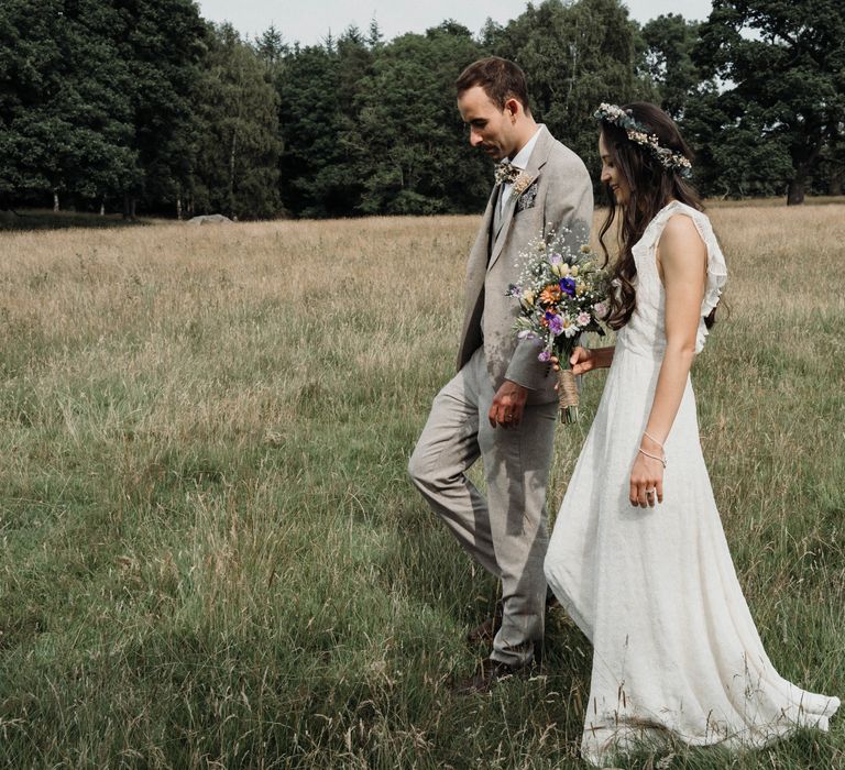 Bride & groom walk through green fields with one another on their wedding day