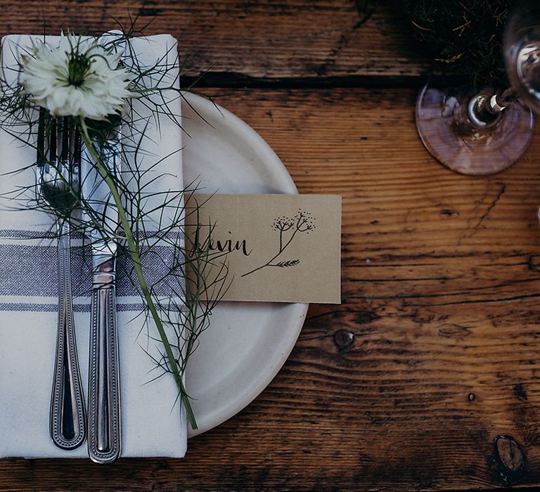 Place setting with napkins, cutlery, flower stem and craft paper name place card 