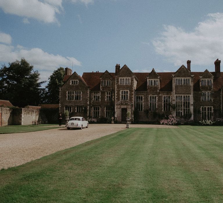 Exterior of Loseley Park with classic white car parked outside on sunny summer day