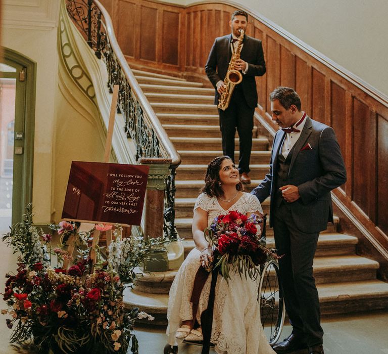 Saxophonist playing music to the bride and groom on the stairs at Dulwich College with acrylic wedding sign and floral arrangement decor