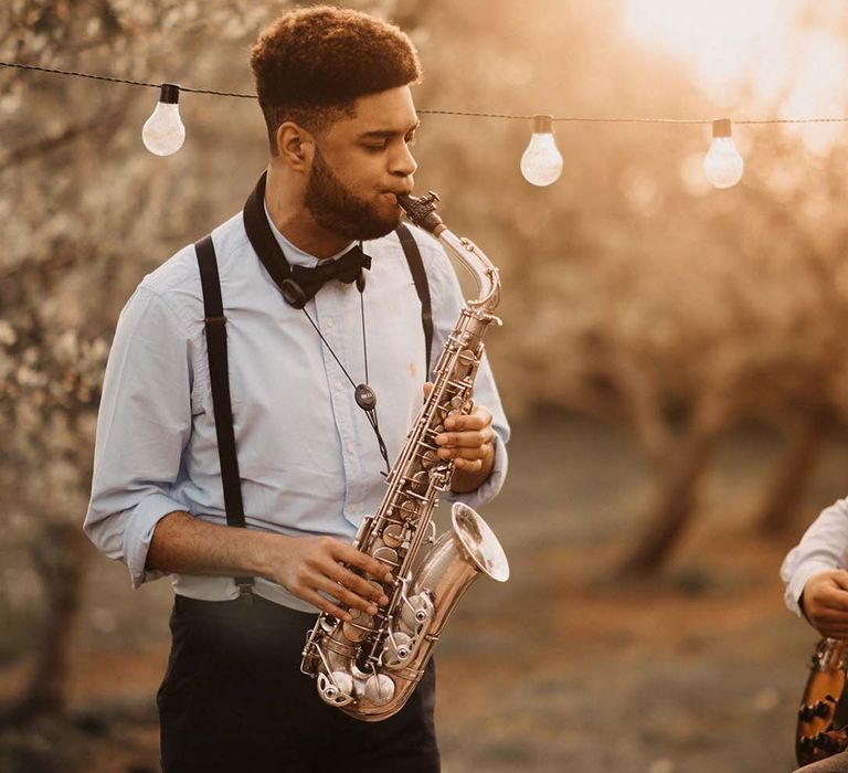 Saxophonist playing music at the outdoor first dance under a canopy of festoon lights 