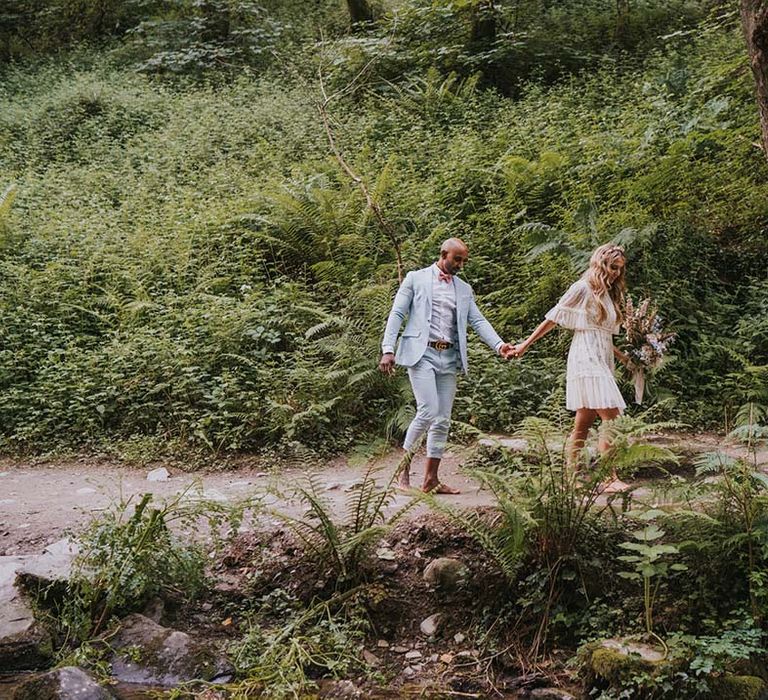 Bride & groom hold hands as they walk through the woodland in Cornwall