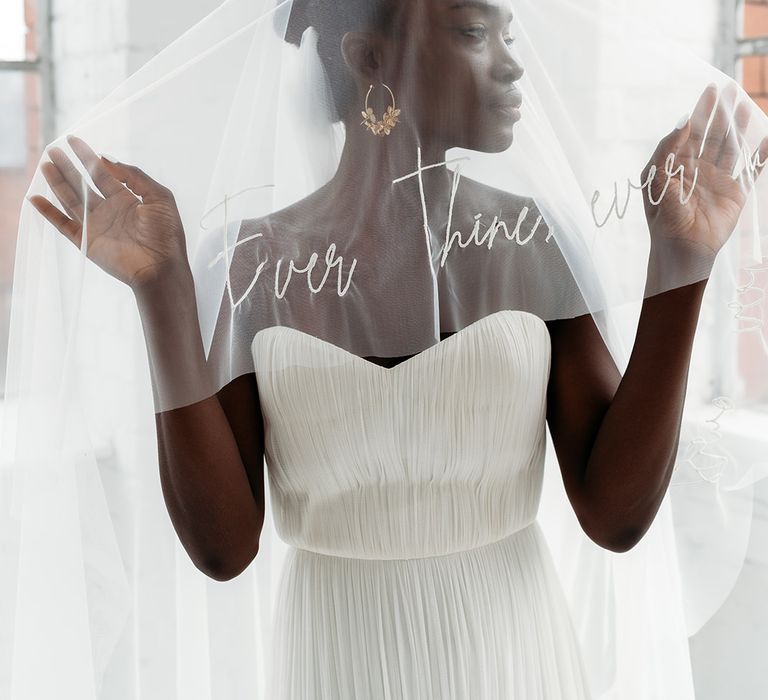 Black bride in a strapless wedding dress with stunning afro hair up do holding our her 'Ever Thine, Ever Mine' personalised veil