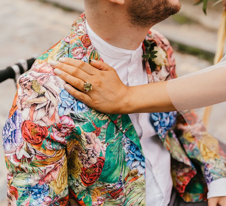 Bride wearing a Peridot engagement ring with white nail polish resting her hand on her grooms shoulder in a patterned blazer 