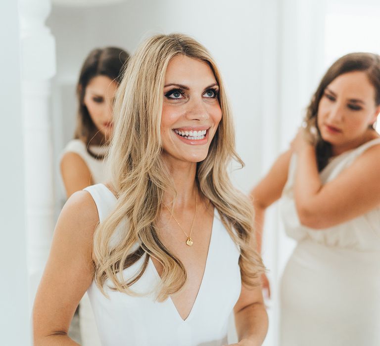 Blonde bride smiling with long flowing hair, grey smokey eye make up and clear glossy lipstick