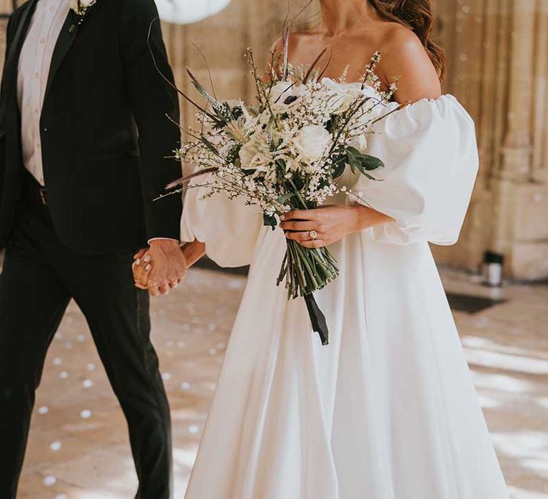 Bride in a strapless wedding dress with detachable puff sleeves holding a white wedding bouquet with roses, astilbe and anemones 