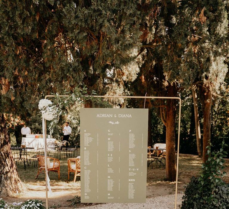 Table plan on green stationery with white writing hangs on metal complete with floral foliage decor | Royal Studio