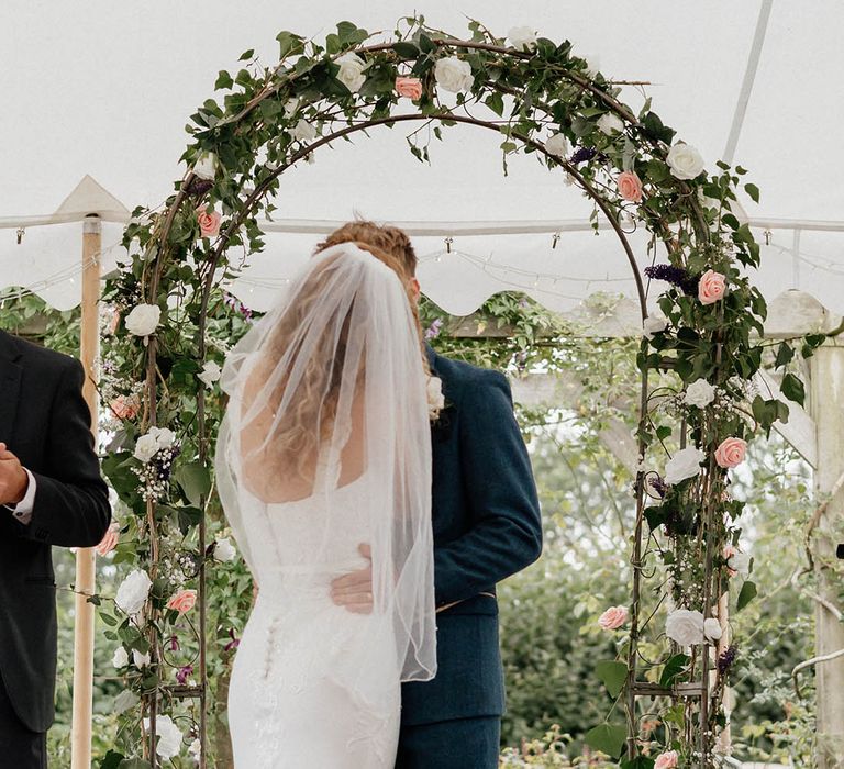 Bride & groom meet each other under floral archway during wedding ceremony