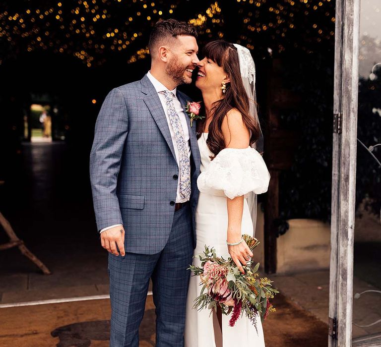 Bride & groom embrace and laugh with one another as bride holds colourful floral bouquet and wears Rime Arodaky dress complete with Miu Miu platform sandals