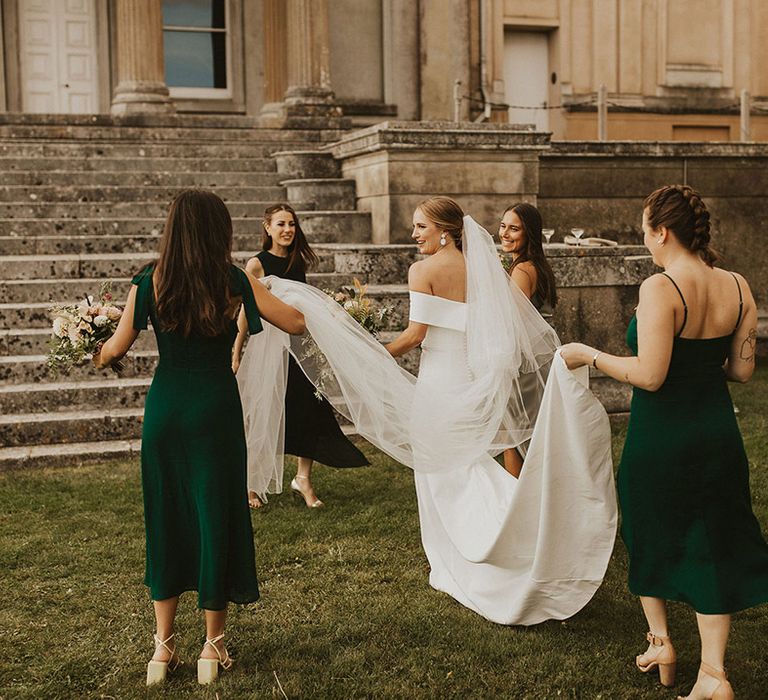 Bride has help from bridesmaids as they hold her bridal gown on wedding day