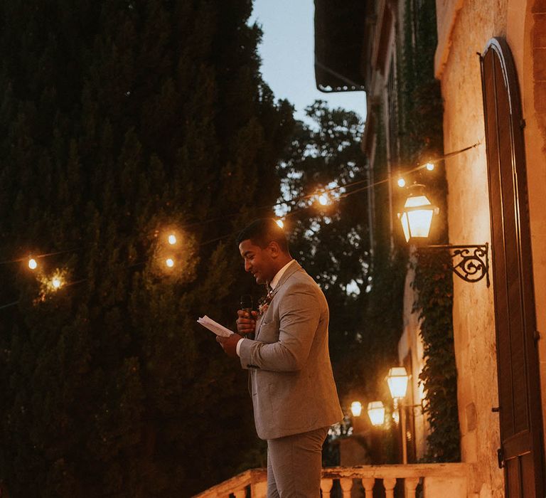 Groom stands outdoors on balcony with candles 