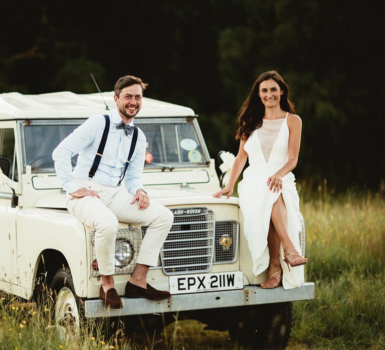 Bride & groom sit on white Defender on their wedding day