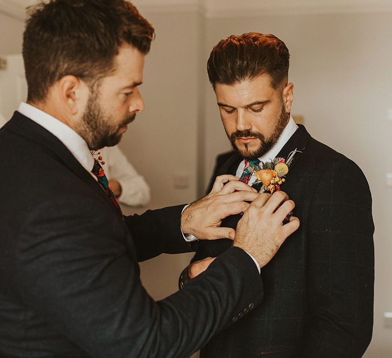 Best man putting on the grooms colourful flower buttonhole flower 