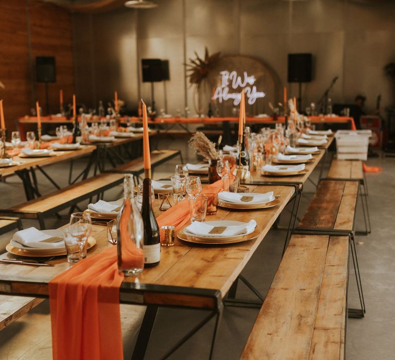 Rustic barn wedding reception with orange table runner, orange dinner candles and long wooden tables and benches 