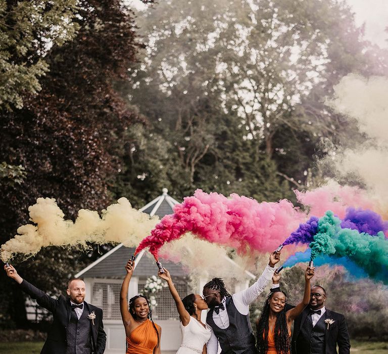 Bride & groom stand with their wedding guests as they let off colourful smoke bombs