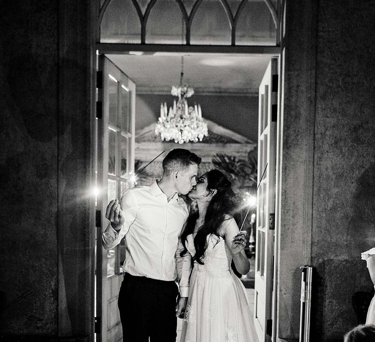 Bride & groom kiss as they hold sparklers in black & white image