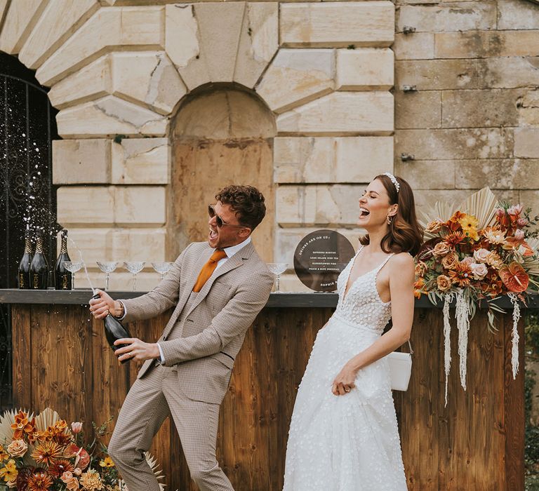 Fun wedding photography of the bride and groom popping champagne in a beige check suit and princess wedding dress 