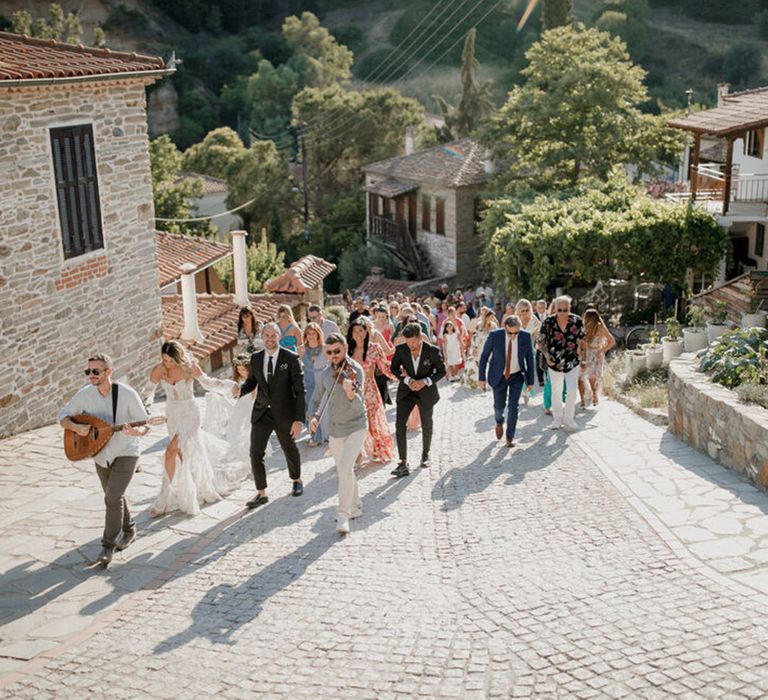 Wedding guests walk outdoors together whilst band plays 