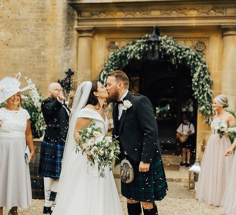 Confetti moment with Bride in a Suzanne Neville princess wedding dress kissing her groom in a tartan kilt at Foxhill Manor 