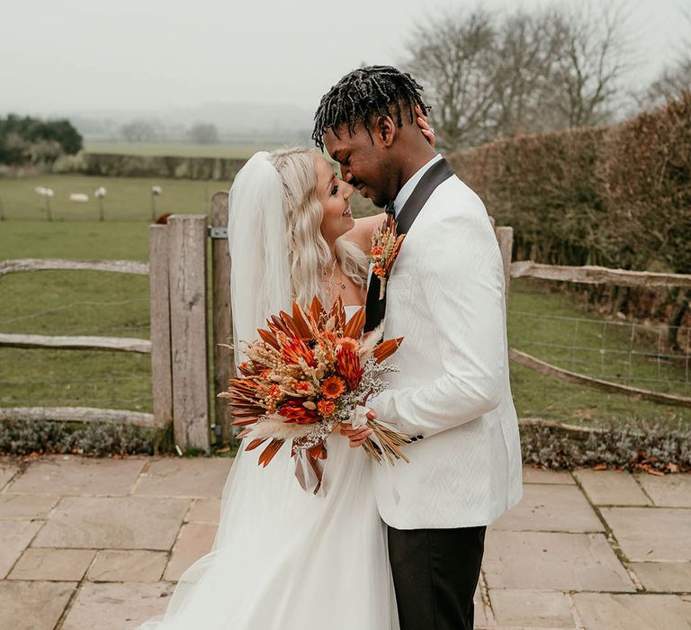 Bride in gold wedding crown embraces groom in white tuxedo