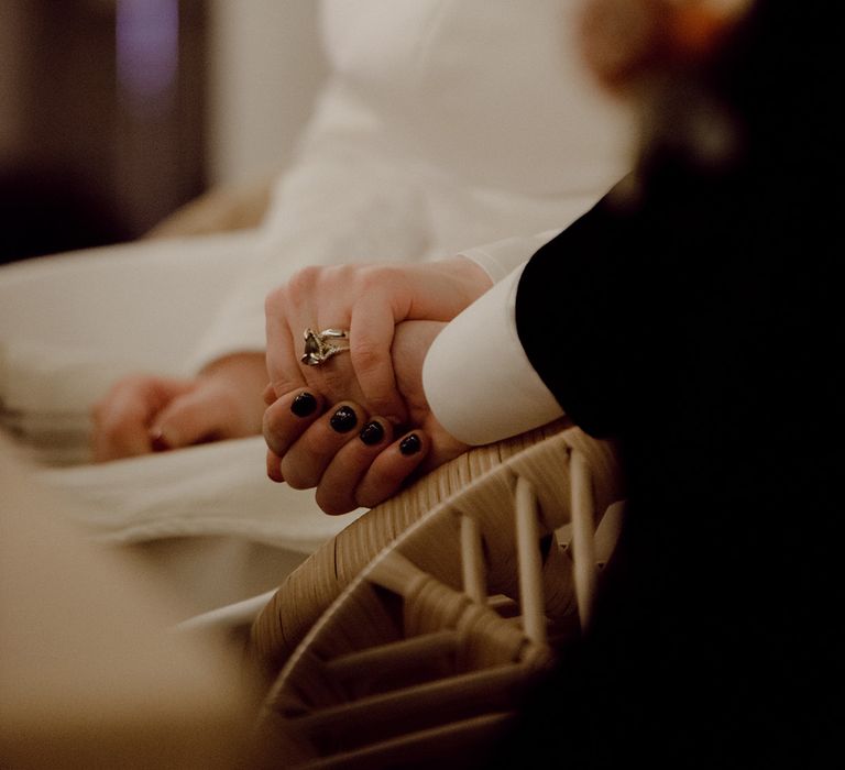 Close-up of the bride and groom holding hands with black nail polish and silver jewellery 