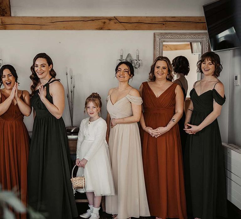 Bridesmaid in earth toned dresses with various neckline styles and flower girl in white dress with woven basket 