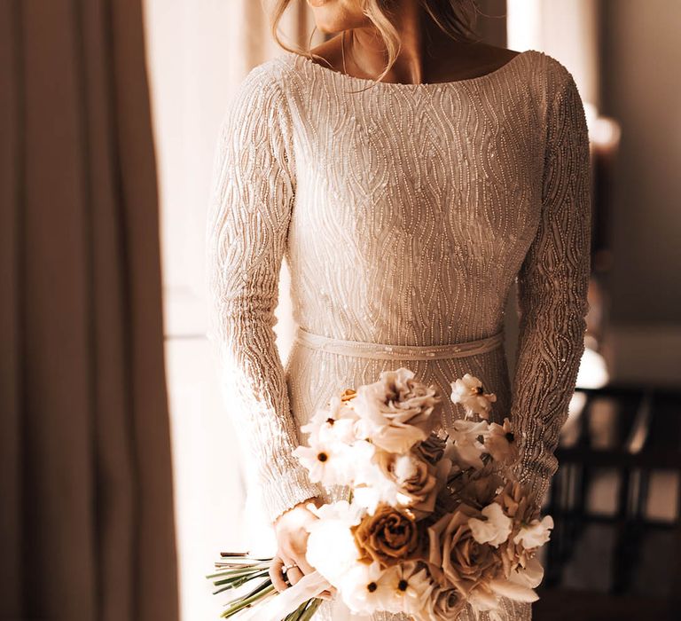 Bride with updo and wispy pieces hairstyle with beaded wedding dress and neutral wedding bouquet