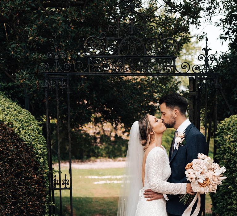 Bride in long sleeve beaded wedding dress kisses groom in dark blue suit at Pennard House on their wedding day 