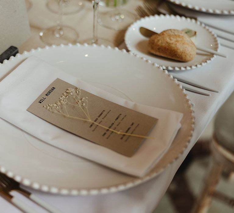 White plates and napkins with cardboard name place card and menu with dried flower 