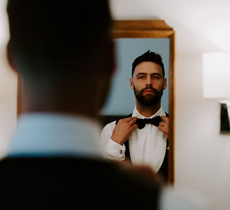 Groom puts on his bow tie for black tie wedding