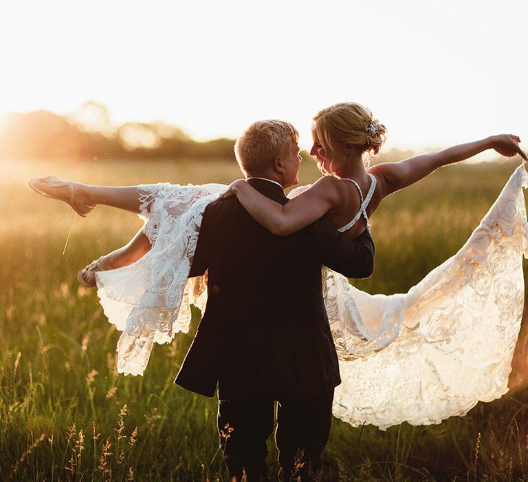 Groom lifts bride in princess lift as her lace boho dries flies around her with sparkly flat sandals 